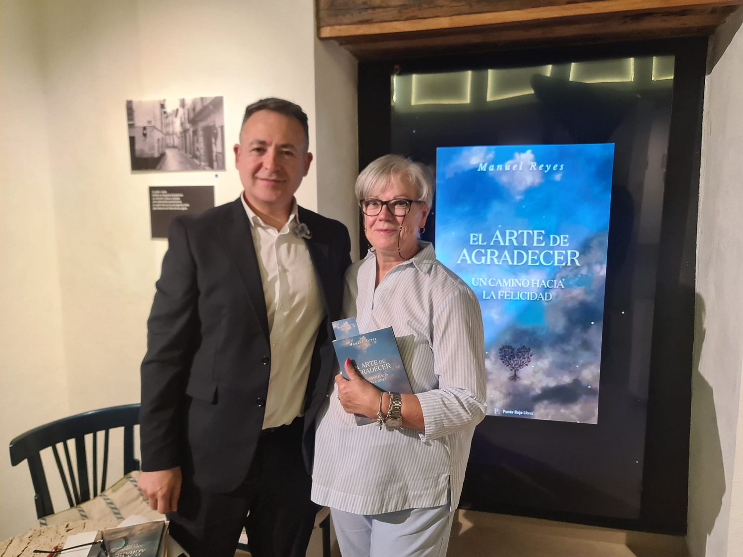 Manuel Reyes junto a una asistente que sostiene un ejemplar del libro, delante de la pantalla con la portada